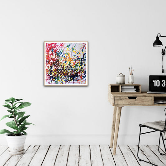 Flecks of Sunlight original fluid acrylic abstract painting by Diana Dimova TRAXI ART. Distinction Award winner 2025, San Francisco. A square framed abstract art print with colorful paint splatters hangs on a white wall in a styled room setting with a wooden desk, lamp, and potted plant.