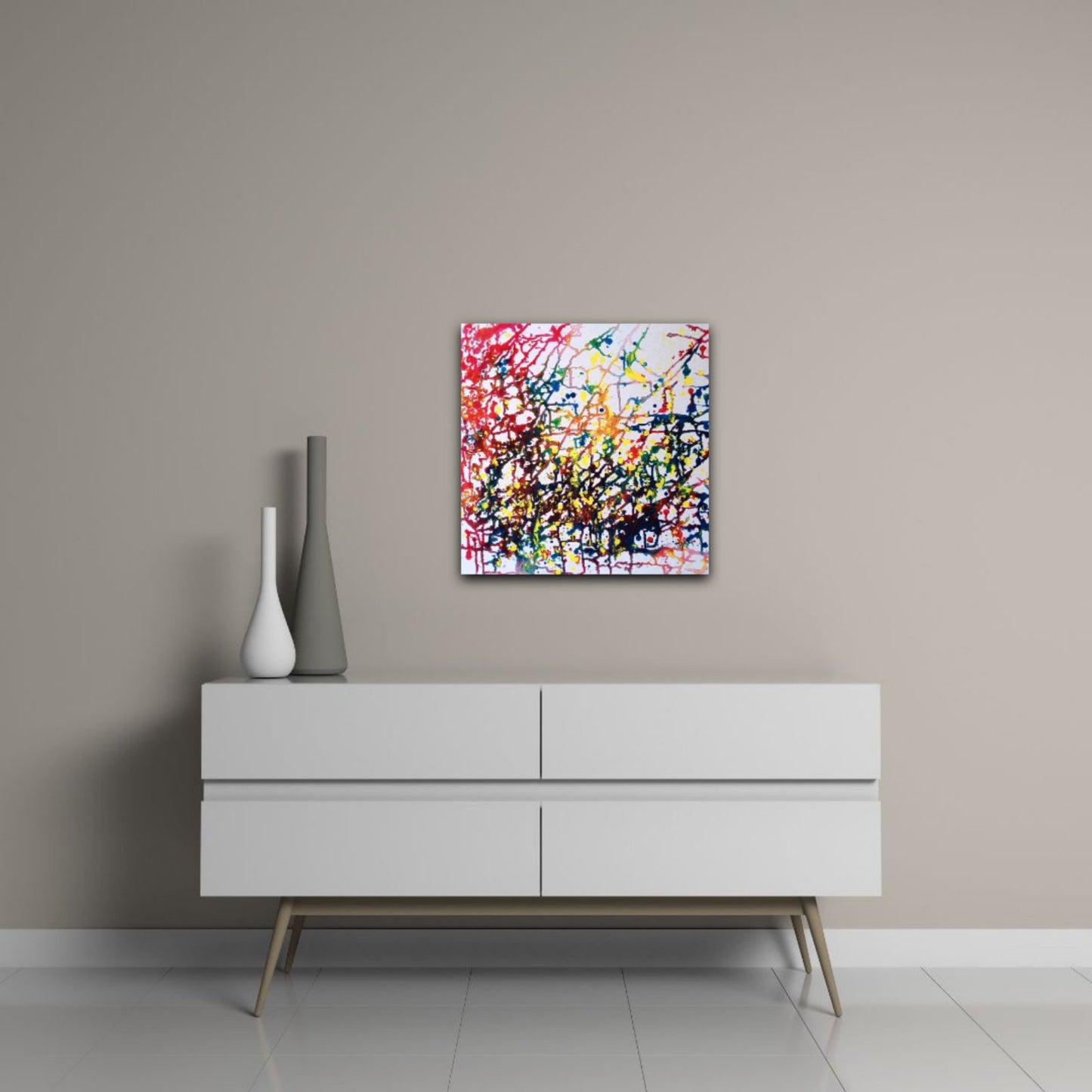 Flecks of Sunlight original fluid acrylic abstract painting by Diana Dimova TRAXI ART. Distinction Award winner 2025, San Francisco. A square abstract canvas print with vibrant multicolored paint splatters hangs on a beige wall above a modern white sideboard with decorative vases.