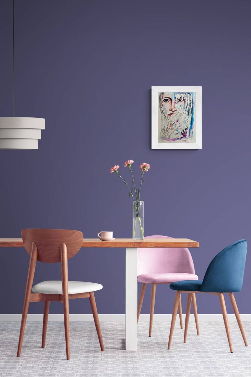 A modern dining room scene with a wooden table, three upholstered chairs in brown, pink, and blue, a glass vase with pink flowers, and a framed abstract portrait on a purple wall. Frozen original emotional watercolor portrait of a woman in blue and white tones by Diana Dimova TRAXI ART.