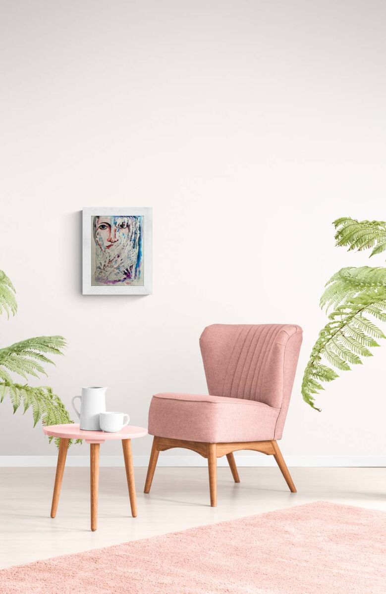 A pink upholstered accent chair with wooden legs sits in a bright room next to a small pink side table with white cups, with a framed abstract portrait on the wall and green plants framing the scene. Frozen original emotional watercolor portrait of a woman in blue and white tones by Diana Dimova TRAXI ART.