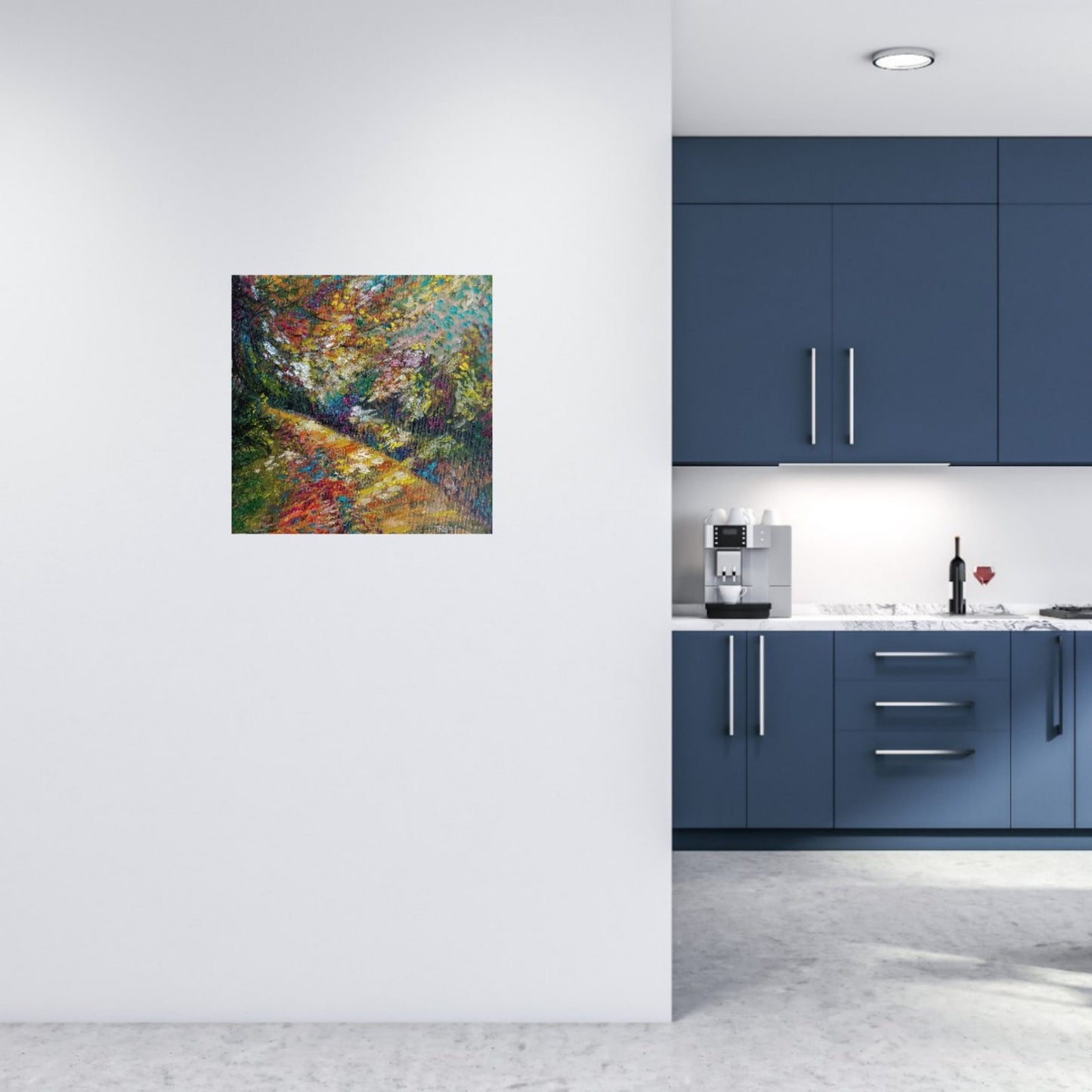 A square colorful painting of a forest path hangs on a white wall in a modern kitchen with dark blue cabinets and a light gray floor. Impression in Autumn Colors original abstract impressionist oil painting with blue, yellow, orange, and red tones by Diana Dimova TRAXI ART.
