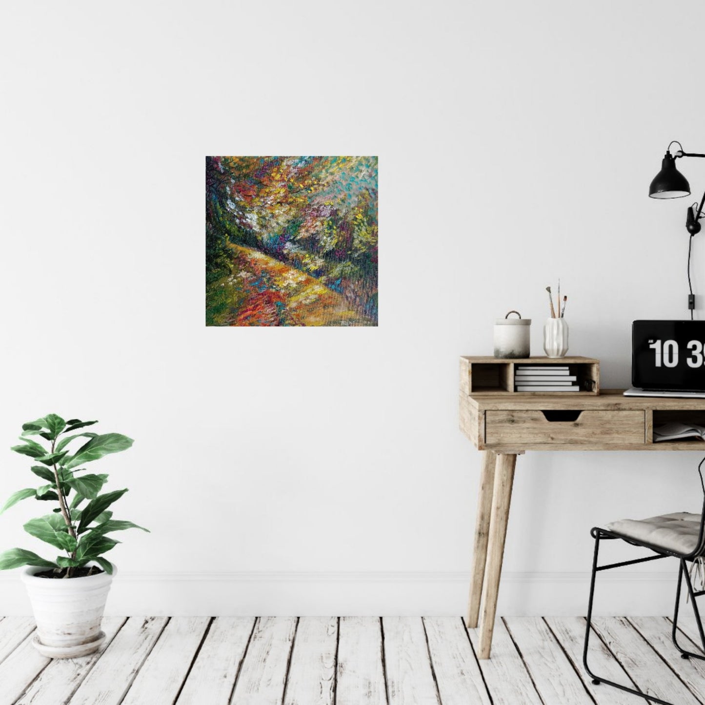 A colorful abstract landscape painting is displayed on a white wall in a styled room setting with a wooden desk, black lamp, and a potted green plant on a white wood floor. Impression in Autumn Colors original abstract impressionist oil painting with blue, yellow, orange, and red tones by Diana Dimova TRAXI ART.