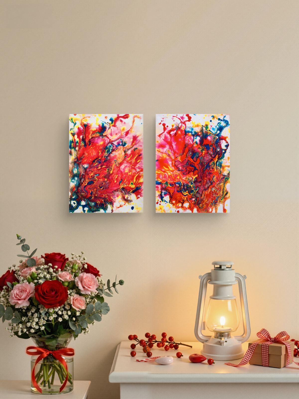 Magic Set original expressive red abstract diptych with fluid acrylic shapes by Diana Dimova TRAXI ART. Two square abstract canvas prints with vibrant red, pink, orange, blue, and white brushstrokes hang on a beige wall above a white table styled with a flower bouquet, a lit lantern, and a small gift box.