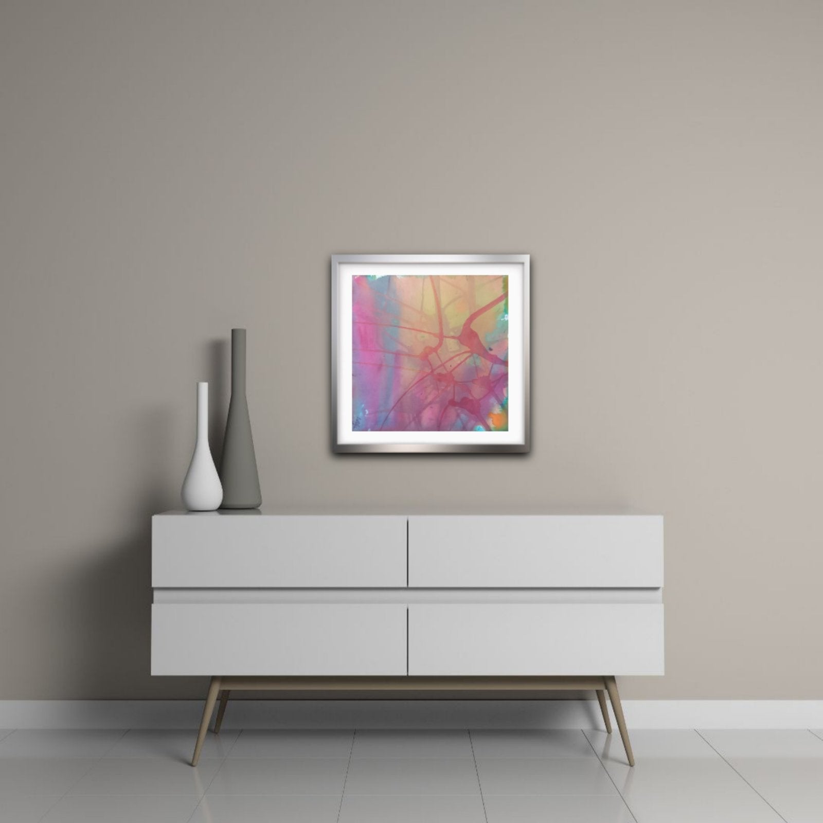  Nuances of Time original abstract mixed media square painting with soft pastel pink and violet tones by Diana Dimova TRAXI ART. A square framed abstract art print with vibrant pink, purple, orange, and yellow brushstrokes, displayed on a light gray wall above a modern white sideboard with decorative vases.