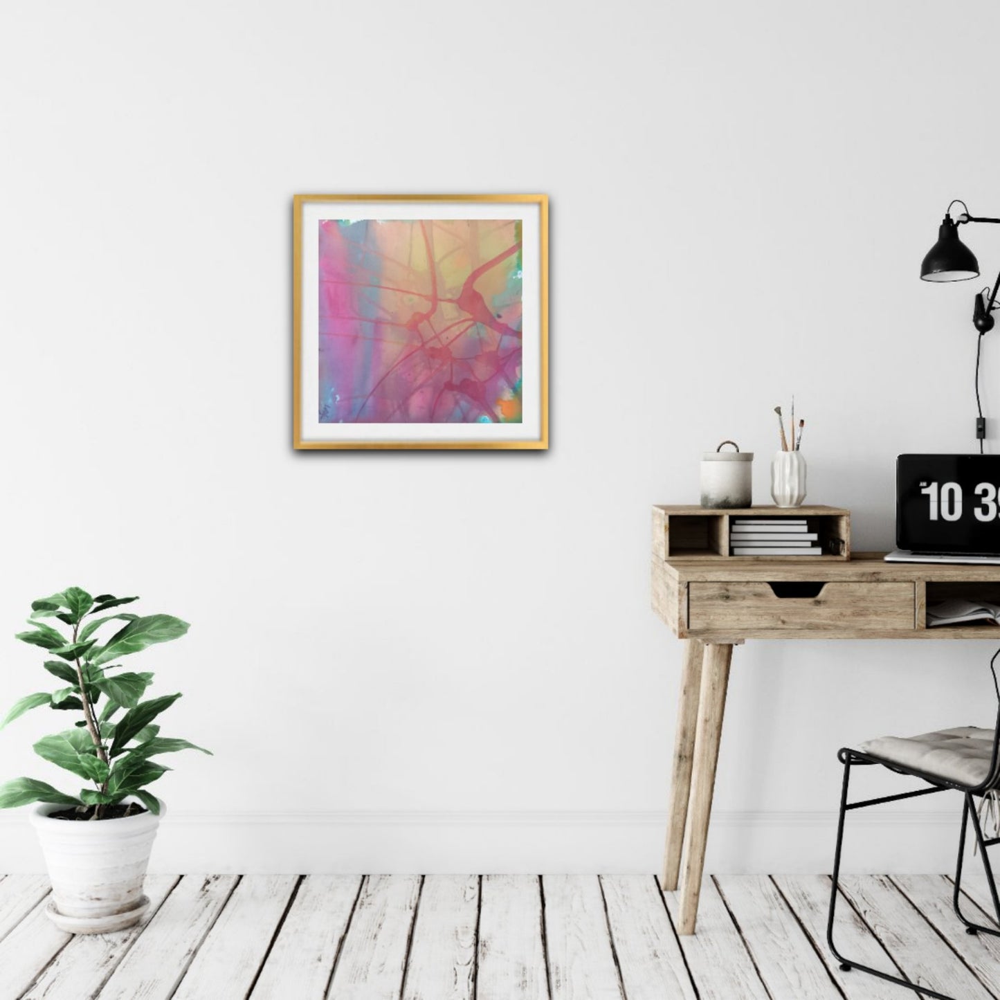 Nuances of Time original abstract mixed media square painting with soft pastel pink and violet tones by Diana Dimova TRAXI ART. A framed abstract art print with vibrant pink, purple, and yellow brushstrokes hangs on a white wall in a modern, minimalist room with a wooden desk, black lamp, and a potted green plant.