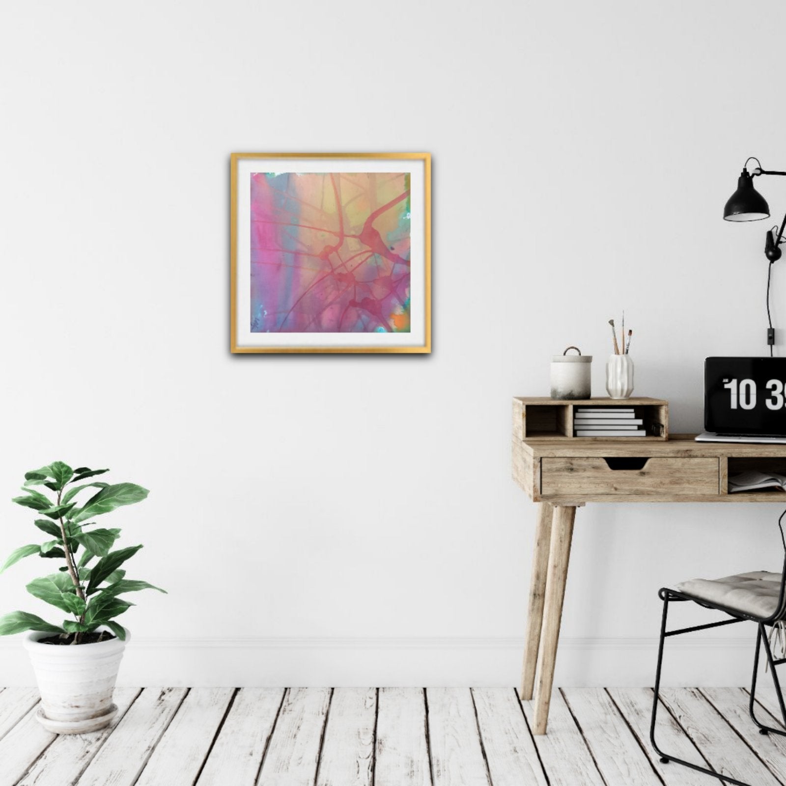 Nuances of Time original abstract mixed media square painting with soft pastel pink and violet tones by Diana Dimova TRAXI ART. A framed abstract art print with vibrant pink, purple, and yellow brushstrokes hangs on a white wall in a modern, minimalist room with a wooden desk, black lamp, and a potted green plant.
