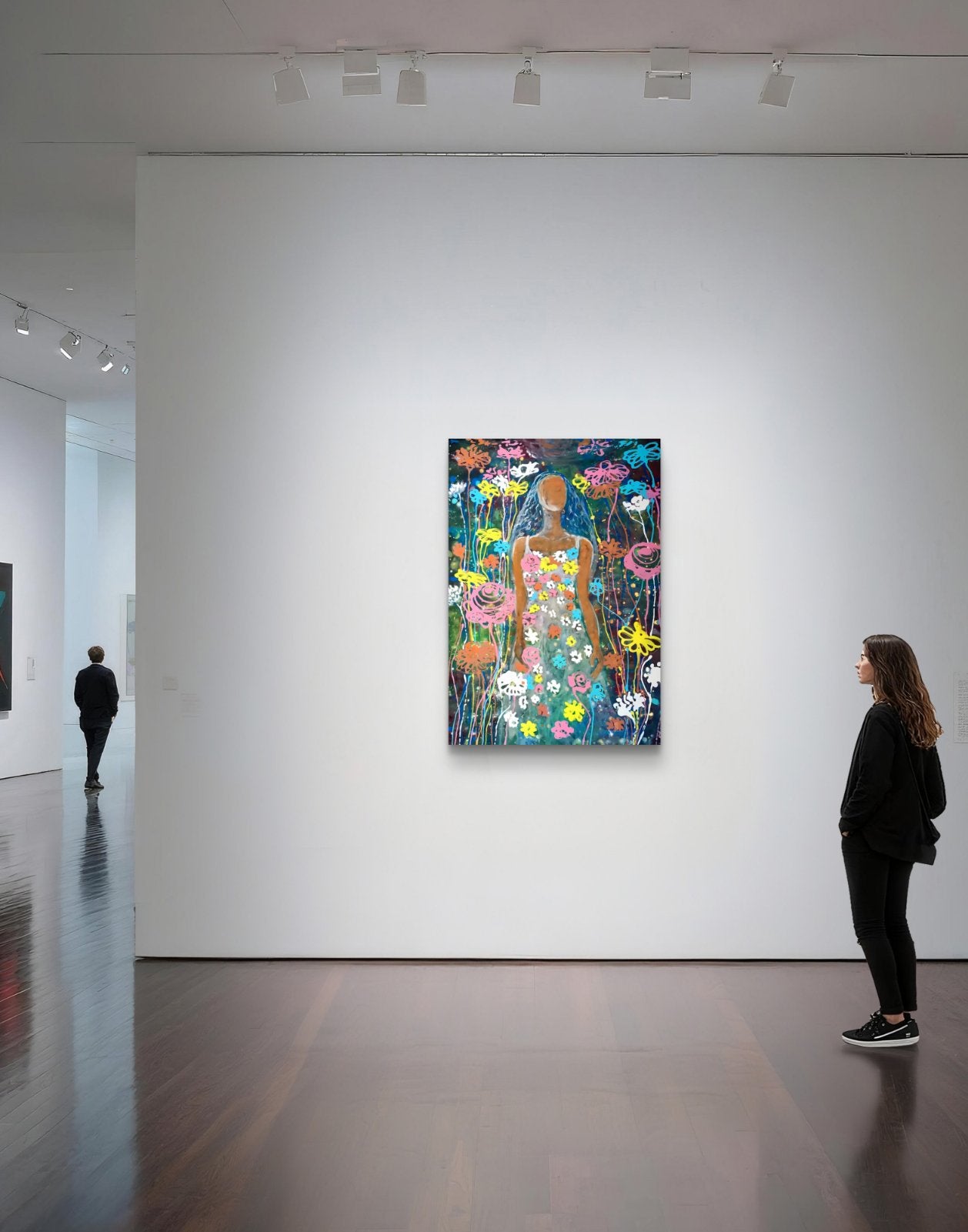 A colorful floral art print featuring a stylized female figure in a dress, displayed on a white gallery wall with a woman looking at it and track lighting overhead. Palm Sunday original spring abstract fluid acrylic painting with vibrant floral colors celebrating feminine energy and Bulgarian heritage by Diana Dimova TRAXI ART.