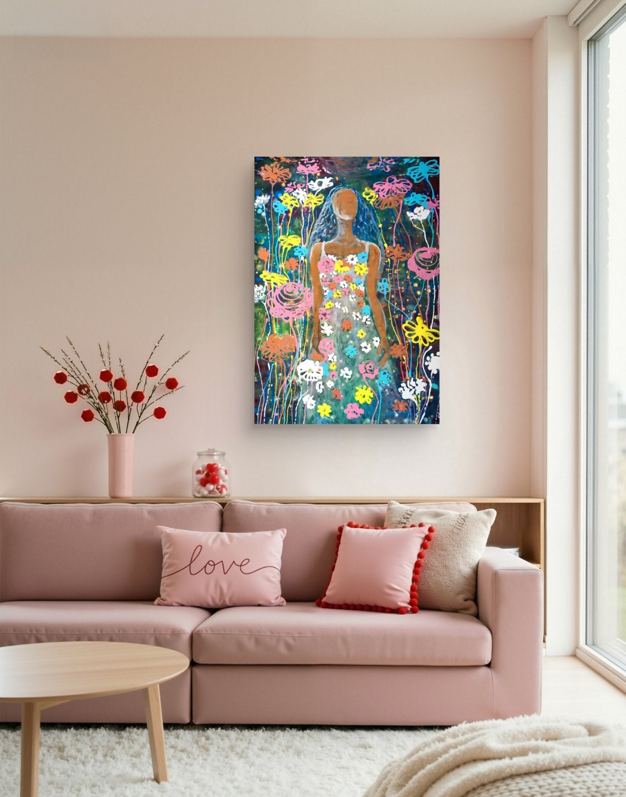 A colorful floral art print featuring a stylized female figure in a dress, displayed on a light pink wall above a pink sofa in a modern living room setting. Palm Sunday limited edition premium vertical canvas print with vibrant floral fluid acrylic colors celebrating feminine energy and Bulgarian heritage by Diana Dimova TRAXI ART.