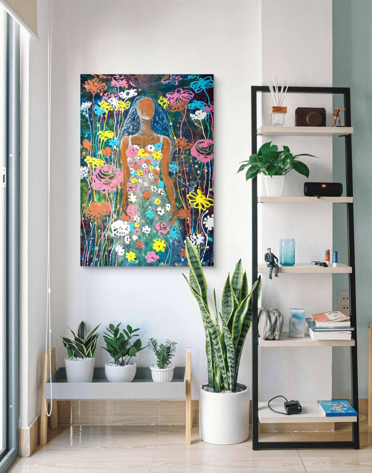 A colorful framed wall art print depicting a stylized figure surrounded by flowers, displayed in a modern interior setting with plants and shelving. Palm Sunday original spring abstract fluid acrylic painting with vibrant floral colors celebrating feminine energy and Bulgarian heritage by Diana Dimova TRAXI ART.