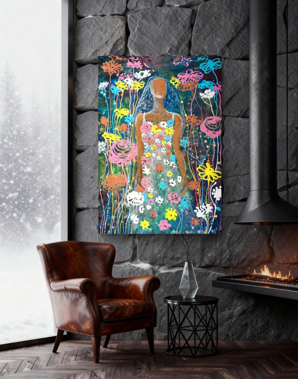 A colorful abstract floral art print featuring a stylized female figure, displayed on a dark stone wall above a brown leather armchair and next to a fireplace in a modern living room setting. Palm Sunday original spring abstract fluid acrylic painting with vibrant floral colors celebrating feminine energy and Bulgarian heritage by Diana Dimova TRAXI ART.