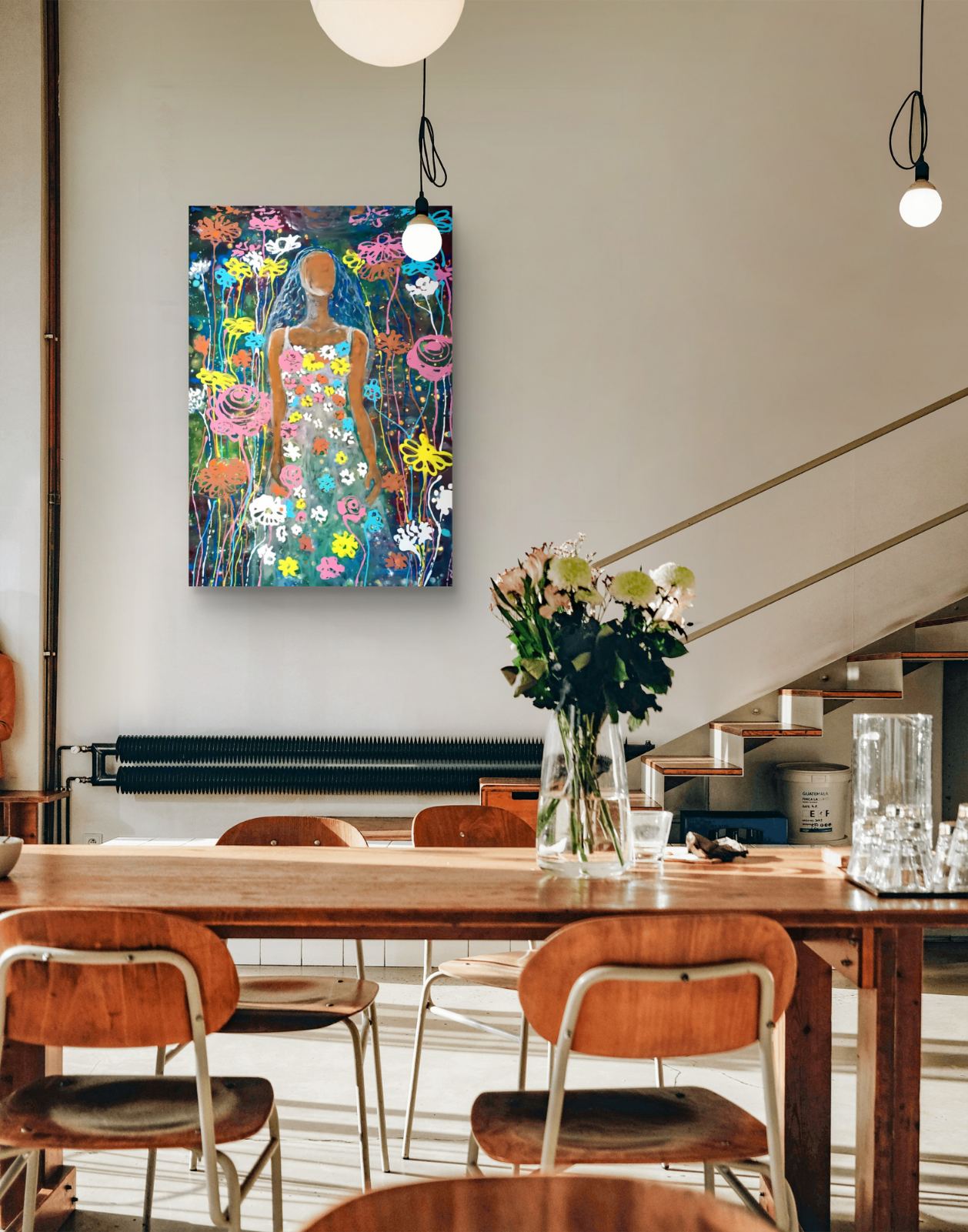 A colorful floral art print featuring a stylized figure in a field of flowers, displayed on a wall in a modern dining room setting with a wooden table and chairs. Palm Sunday original spring abstract fluid acrylic painting with vibrant floral colors celebrating feminine energy and Bulgarian heritage by Diana Dimova TRAXI ART.