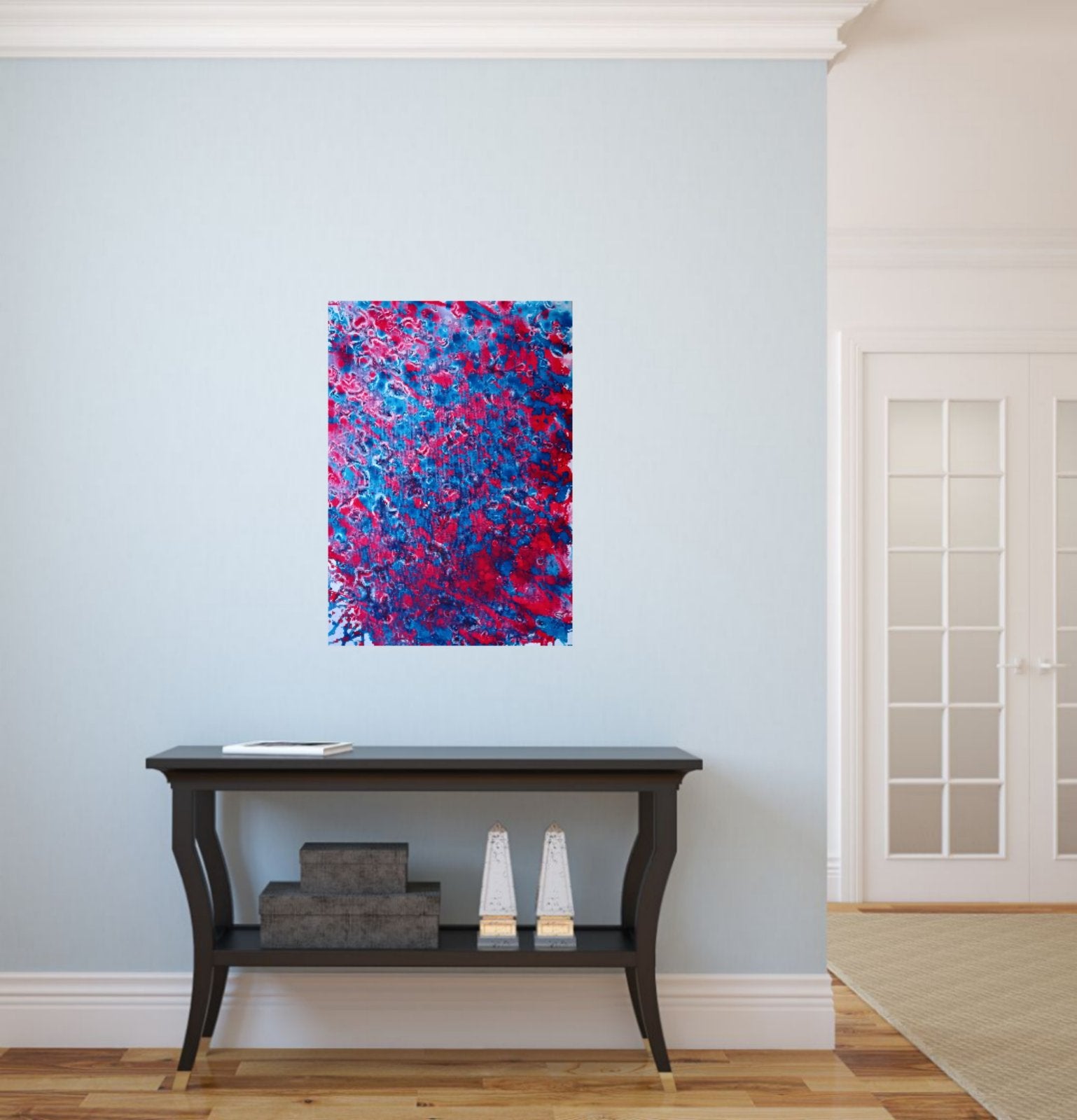 Red & Blue Balance original fluid acrylic abstract painting by Diana Dimova TRAXI ART. An abstract canvas print featuring vibrant red, pink, and blue brushstrokes, displayed on a light blue wall above a dark wood console table in a bright room.