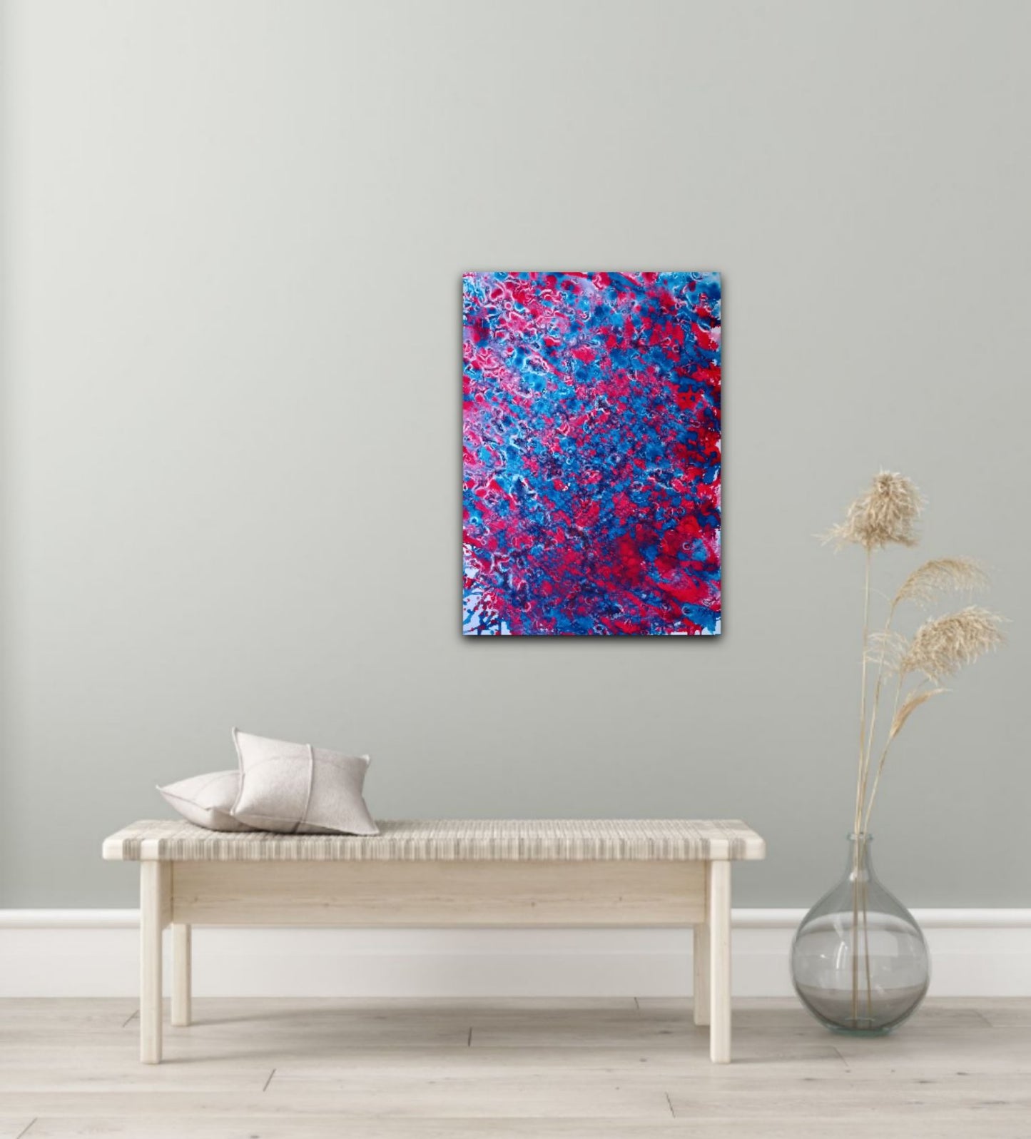 Red & Blue Balance original fluid acrylic abstract painting by Diana Dimova TRAXI ART. Abstract canvas wall art featuring a vibrant mix of blue and red paint splatters, displayed in a styled room setting above a light wood bench with decorative pillows and a glass vase.
