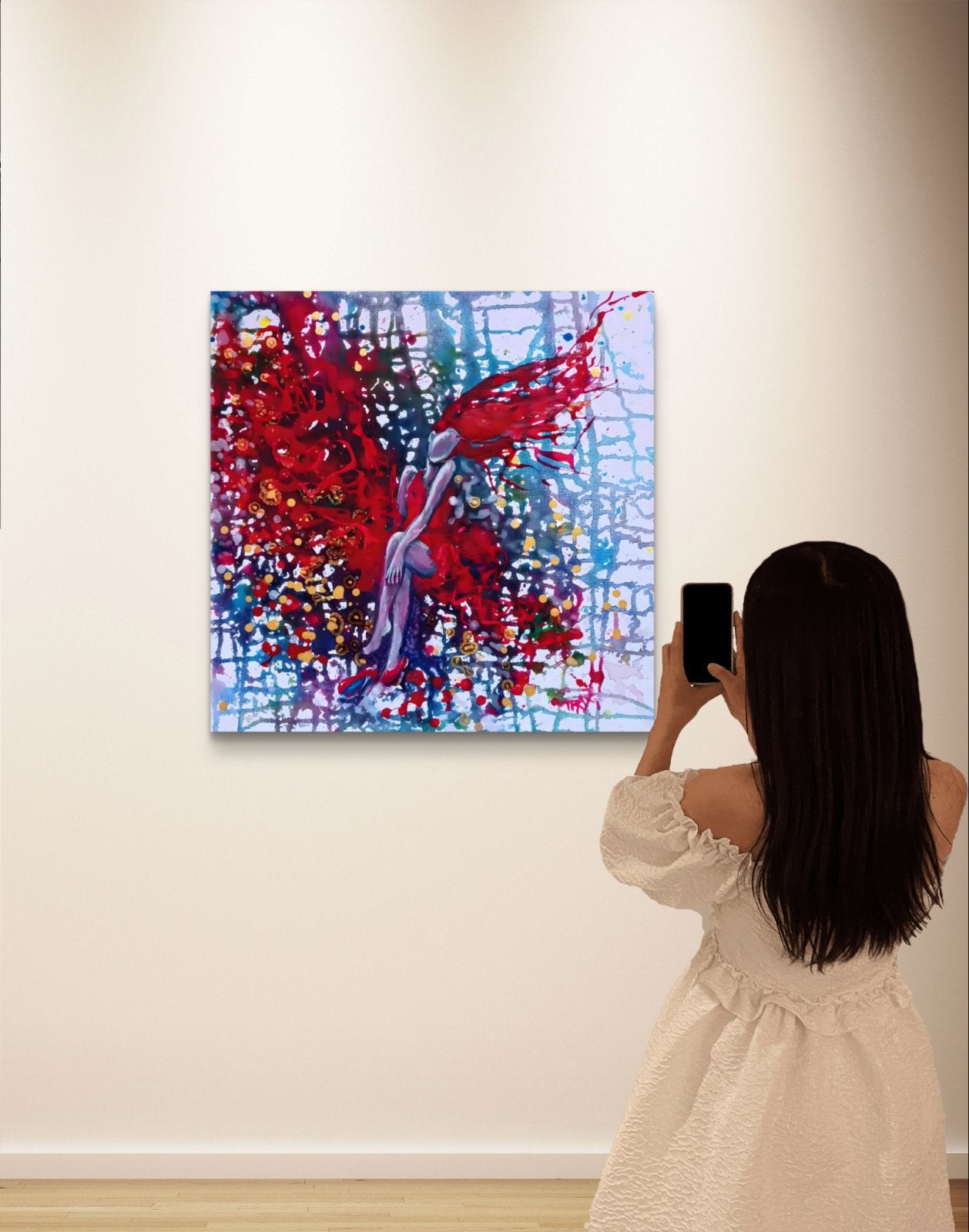 Red Dress & Party Mood original fluid acrylic abstract painting by Diana Dimova TRAXI ART. Finalist Award winner, Camelback Gallery 2025. A woman in a cream dress stands with her back to the camera, holding a smartphone to take a photo of an abstract canvas painting hanging on a white wall. The painting features a dynamic composition of red, blue, purple, and white brushstrokes.