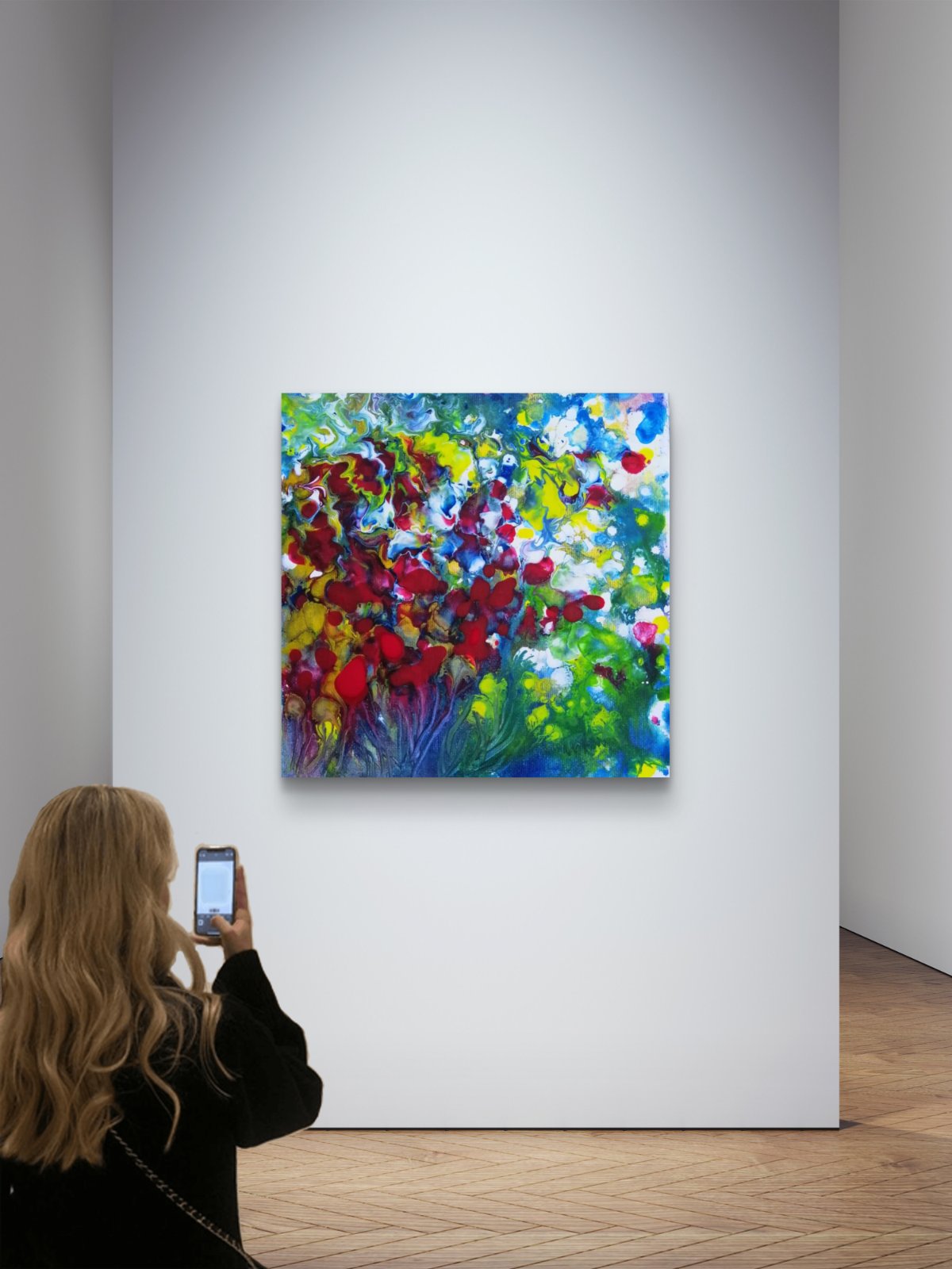A colorful abstract floral painting hangs on a white gallery wall, with a woman taking a photo of it from the side. Red Flowers limited edition premium square canvas print with vibrant red, green, and white fluid acrylic tones by Diana Dimova TRAXI ART.
