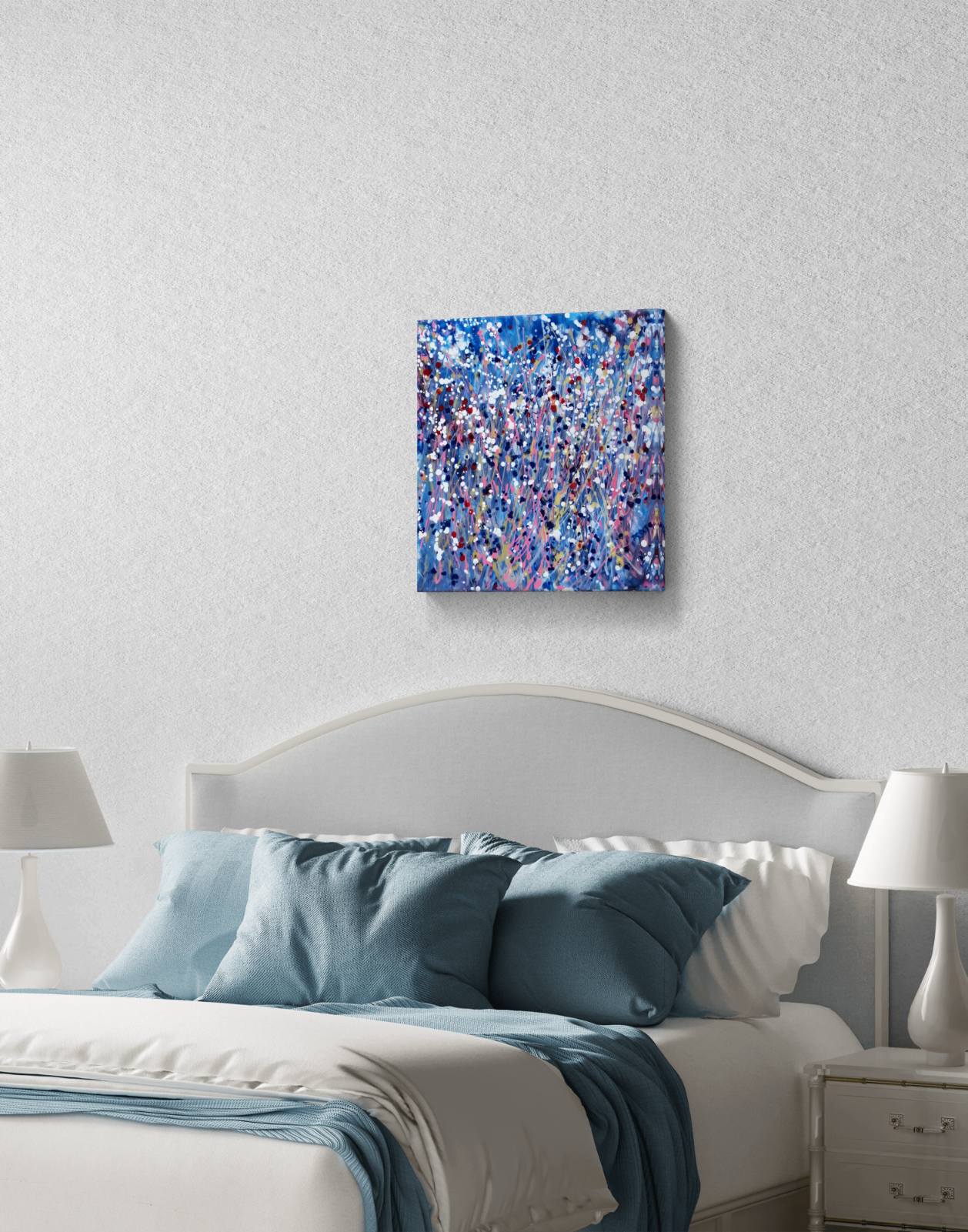 Starlight in the Grass original abstract square painting with calm blue, soft pink, and silver starlight tones by Diana Dimova TRAXI ART. A square abstract canvas print with a vibrant blue, purple, and white paint splatter pattern, displayed on a textured white wall above a bed with blue and white bedding.