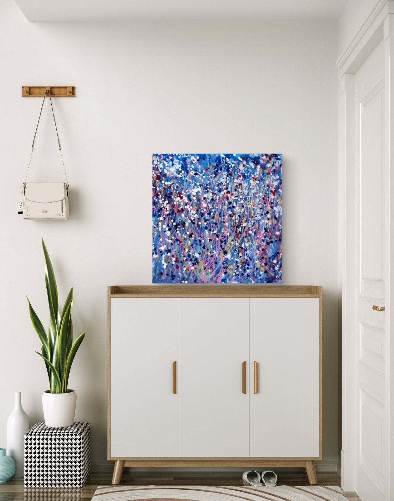 Starlight in the Grass original abstract square painting with calm blue, soft pink, and silver starlight tones by Diana Dimova TRAXI ART. An abstract canvas painting with vibrant blue, purple, and pink brushstrokes displayed on a white wall above a modern white and light wood cabinet in a bright, minimalist room.