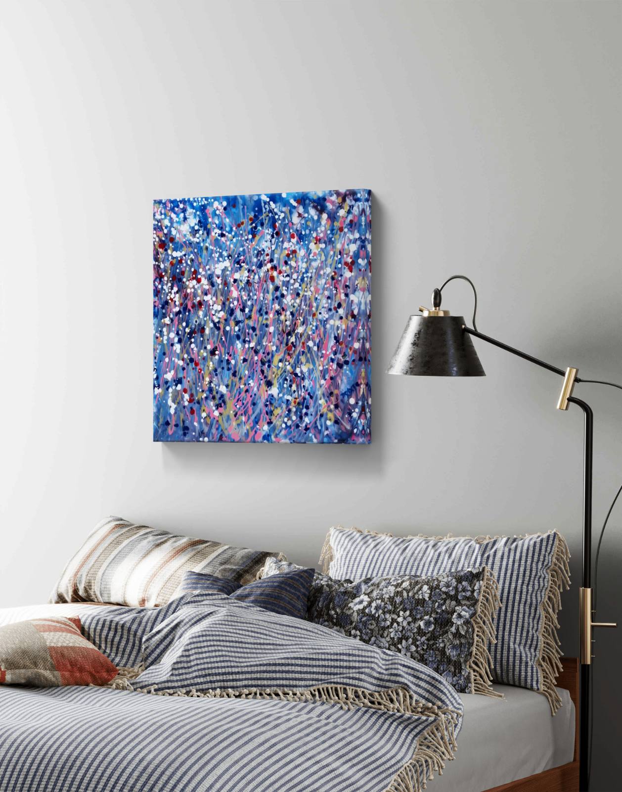 Starlight in the Grass original abstract square painting with calm blue, soft pink, and silver starlight tones by Diana Dimova TRAXI ART. An abstract canvas print featuring a vibrant blue, purple, and white paint splatter design, displayed on a light gray wall above a bed with striped bedding and a black floor lamp.