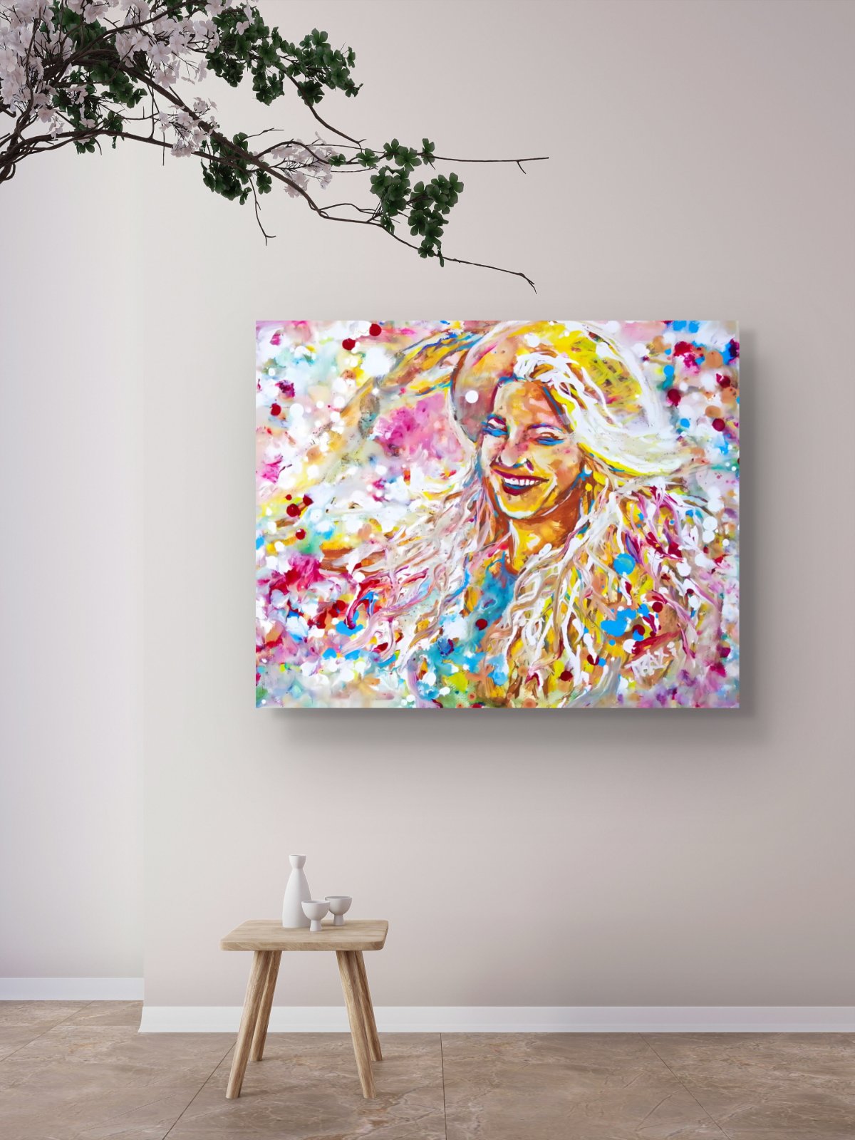 A colorful abstract portrait canvas print of a smiling woman, displayed on a light beige wall above a small wooden stool in a styled room  Sun in the Hair limited edition premium horizontal canvas print depicting a smiling woman in a straw hat with pink and yellow summer light by Diana Dimova TRAXI ART.setting.