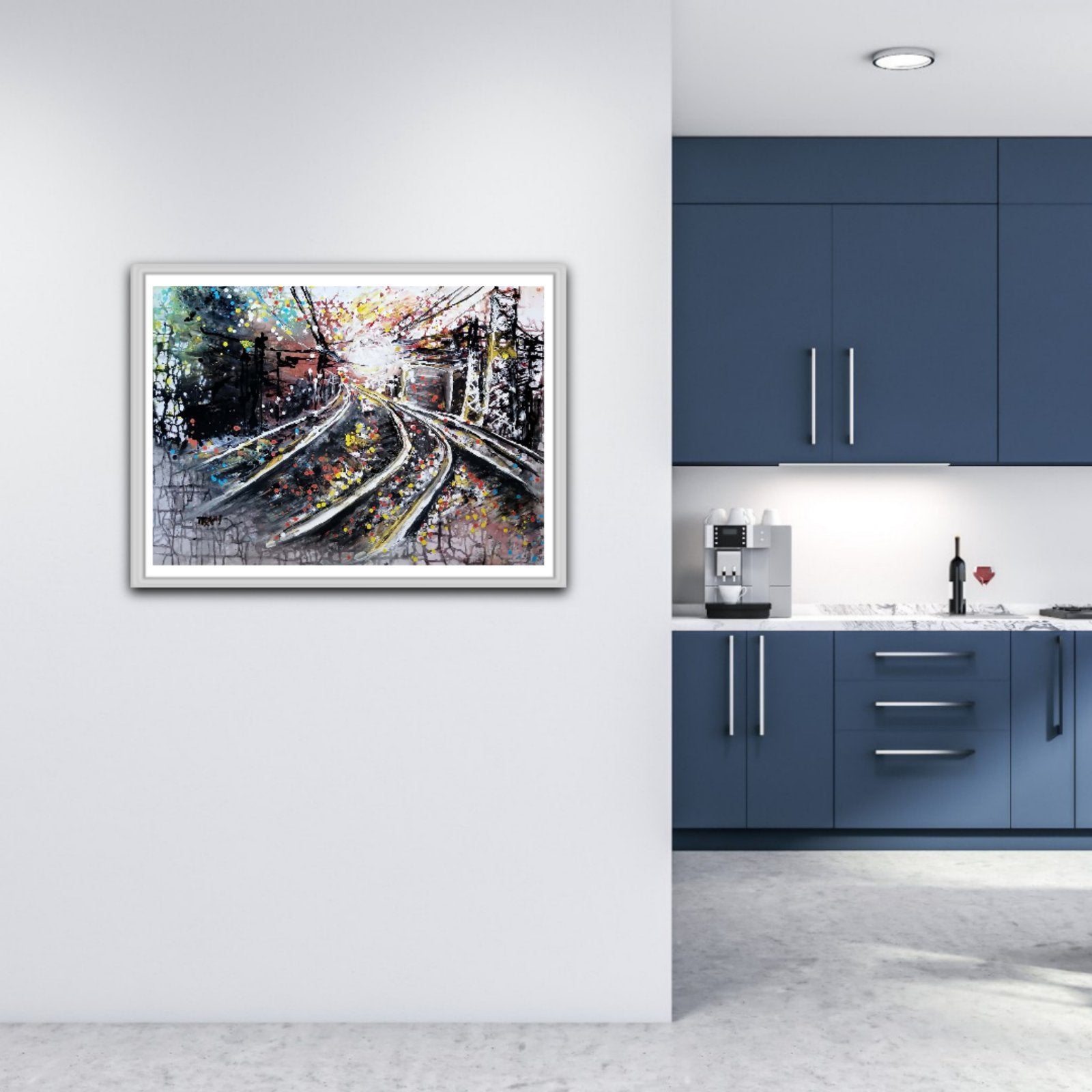 A framed abstract painting of railway tracks is displayed on a white wall in a modern kitchen setting with blue cabinets. The Call of the Rails original abstract urban landscape fluid acrylic painting with minimalist black, brown, and white tones representing railway lines by Diana Dimova TRAXI ART.