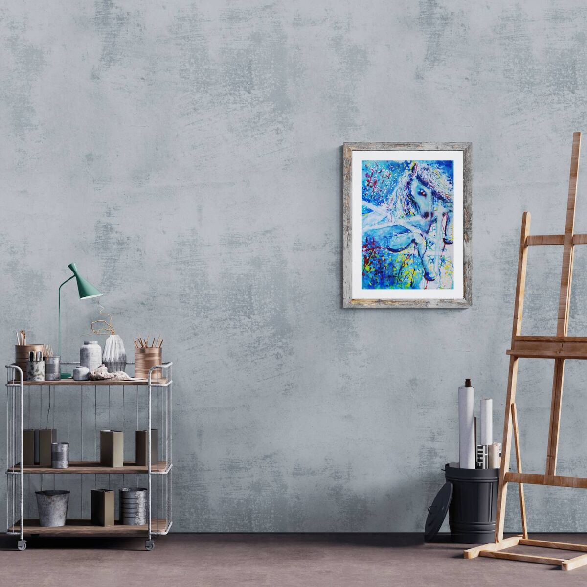 A framed abstract painting of a horse in vibrant blue, white, and purple tones, hung on a textured gray wall in a styled studio setting with an easel and shelves. White Horse and Blue Freedom original symbolic fluid acrylic painting with deep blue, white, and red accents by Diana Dimova TRAXI ART.