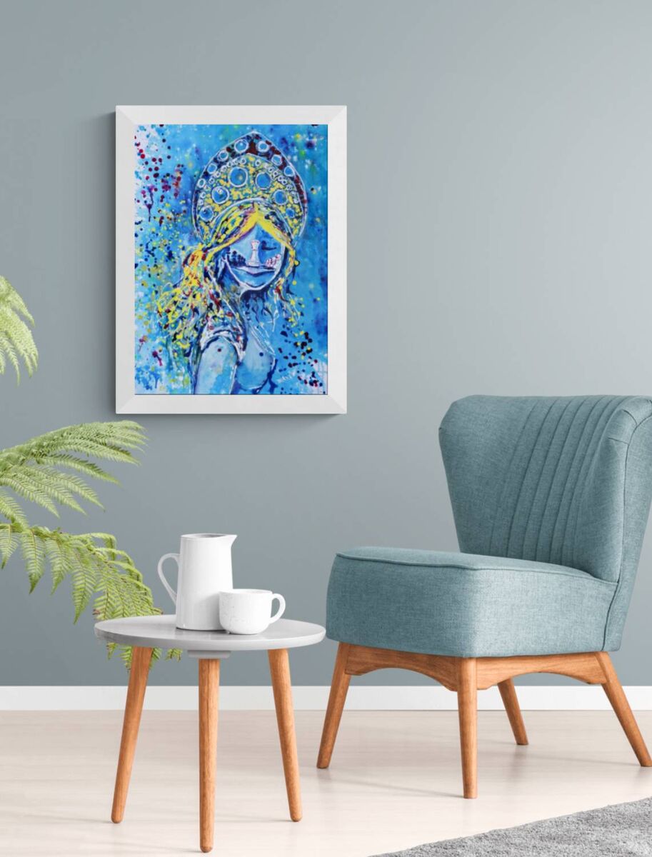 Original spiritual abstract painting titled White Queen’s Move by Diana Dimova TRAXI, featuring a cosmic goddess and chess symbolism in luminous blue and white tones. A framed colorful painting of a woman in a blue and yellow traditional outfit, displayed on a gray wall in a modern living room setting with a teal armchair and a small side table.