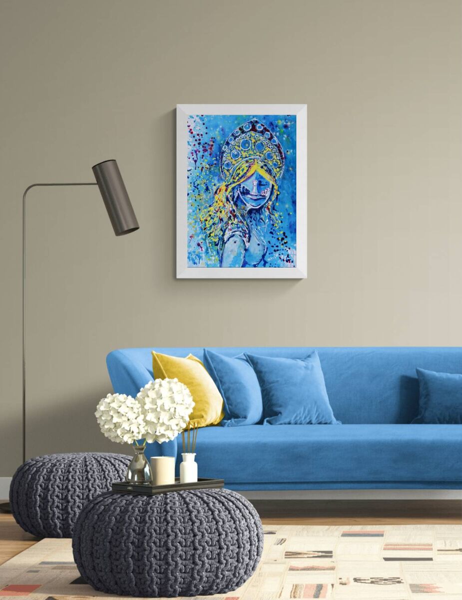 Original spiritual abstract painting titled White Queen’s Move by Diana Dimova TRAXI, featuring a cosmic goddess and chess symbolism in luminous blue and white tones. A framed abstract art print featuring a stylized portrait in vibrant blue and yellow tones, displayed on a beige wall above a blue sofa in a modern living room setting.
