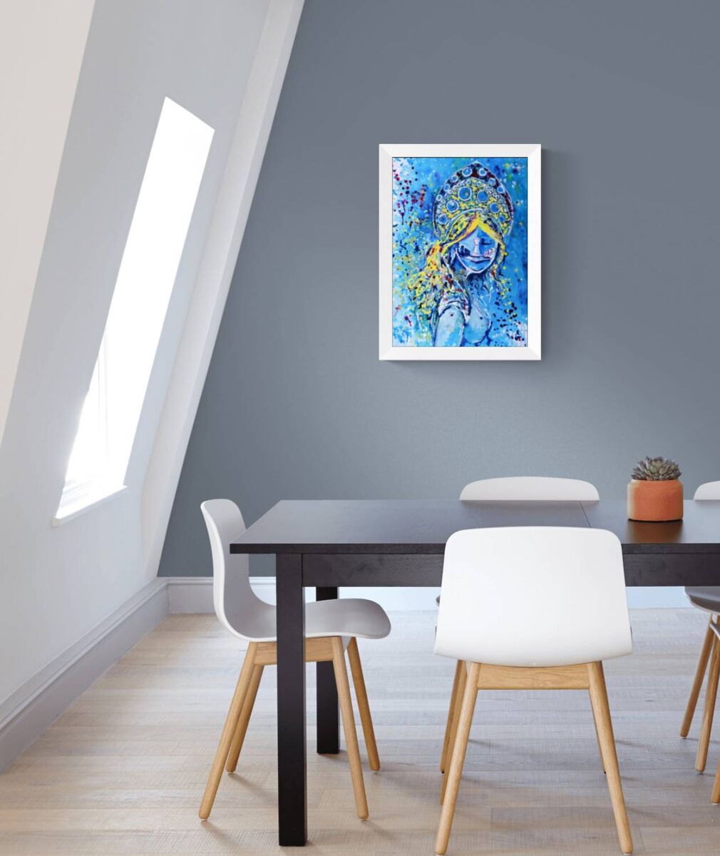 Original spiritual abstract painting titled White Queen’s Move by Diana Dimova TRAXI, featuring a cosmic goddess and chess symbolism in luminous blue and white tones. A framed abstract art print featuring a stylized blue and yellow face hangs on a gray wall above a dining table with white chairs in a modern room.